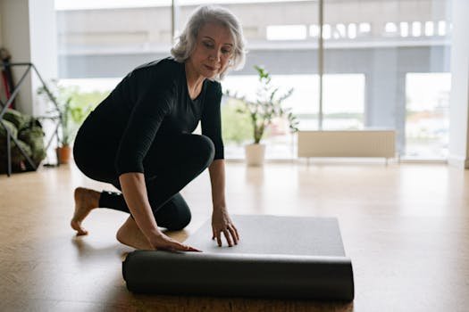 Senior woman setting up yoga mat in bright studio, preparing for exercise.